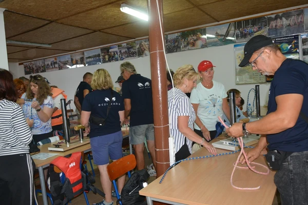 zdjęcie pokazuje uczestników warsztatów żeglarskich w sali ćwiczeń podczas nauki węzłów marynarskich.